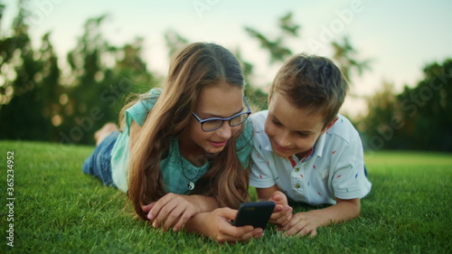 Boy and girl lying on grass with cellphone. Brother and sister using smartphone