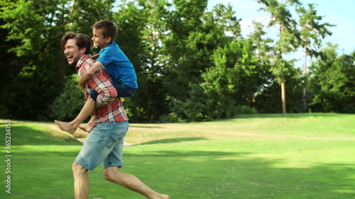 Man running in field with boy on back. Father giving son piggyback riding