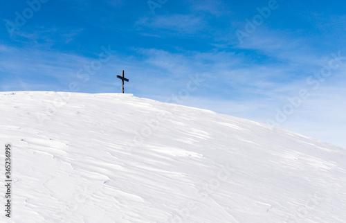 Lonely Summit Cross on windswept snow mountain with blue Sky. Rangiswanger Horn, Alps, Allgau, Bavaria, Germany.
