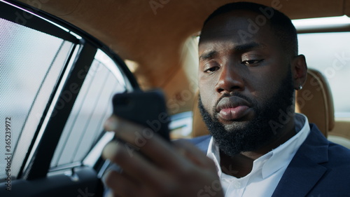 Portrait of focused african business man typing mobile phone at backseat. © stockbusters