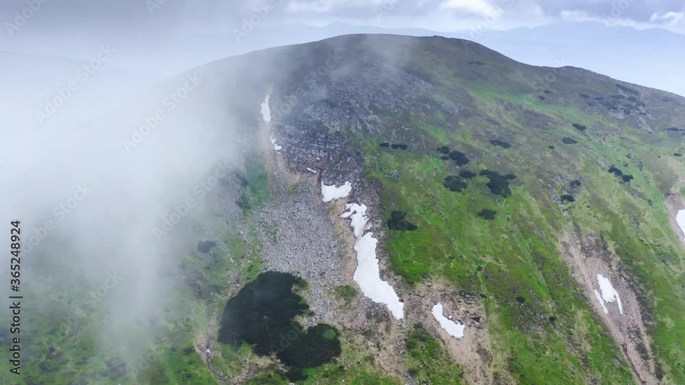 Aerial flight deep inside clouds high above mountain tops. Clouds floating around rocky snowy grassy mountain range. Aerial flight deep inside clouds high above mountain tops. Clouds floating around rocky snowy grassy mountain range.