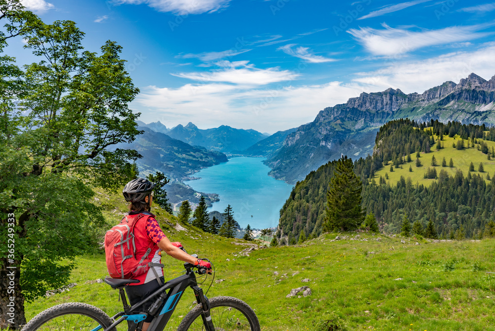 active senior woman riding her electric mountain bike below the seven summits of Churfirsten, enjoying the awesome view down to Lake Walensee Canton St. Gallen, Switzerland