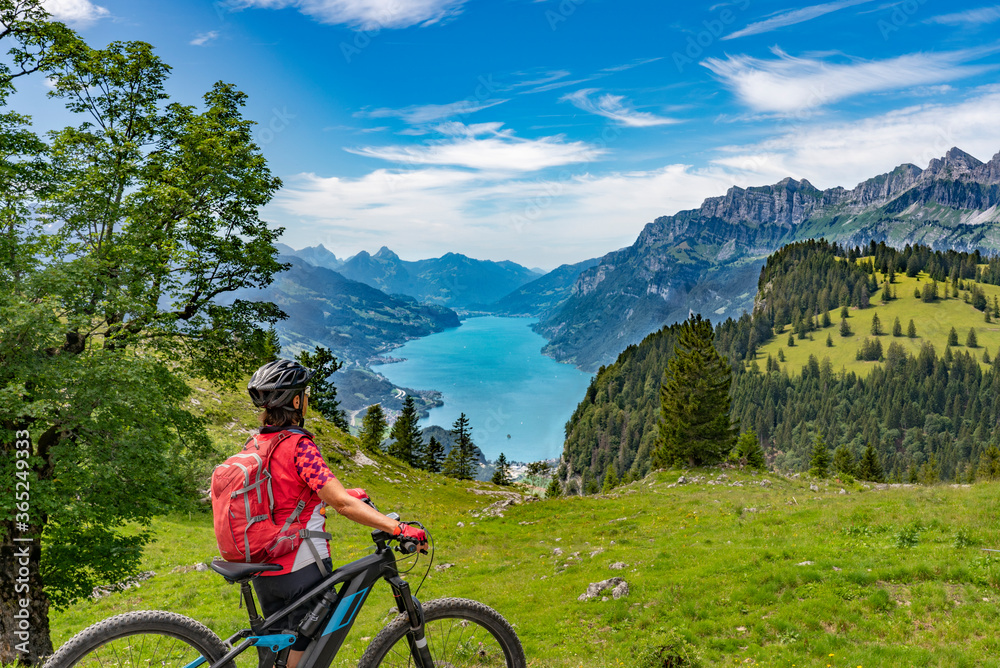 active senior woman riding her electric mountain bike below the seven summits of Churfirsten, enjoying the awesome view down to Lake Walensee Canton St. Gallen, Switzerland active senior woman riding her electric mountain bike below the seven summits of Churfirsten, enjoying the awesome view down to Lake Walensee Canton St. Gallen, Switzerland
