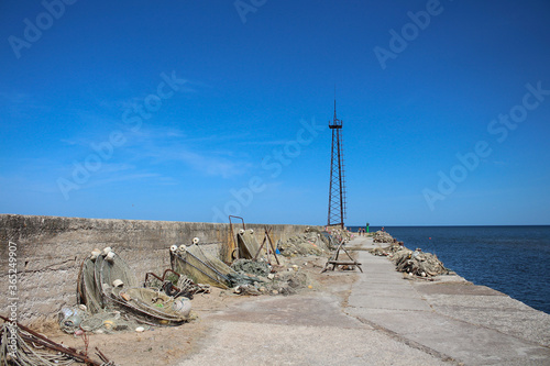  A concrete pier that goes out to sea, with fishing nets on it, and a derrick at the end. Against a bright blue sky...