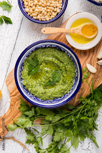 Homemade parsley pesto sauce and ingredients on white wooden background.