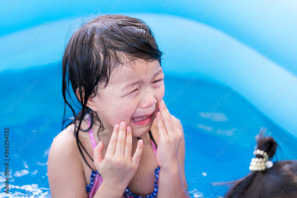 Asian little girl was crying heavily because she was playing in water with her younger sister and crashing. She hurt. The child was wearing a swimsuit, with tears streaming down his cheeks. Wet child.