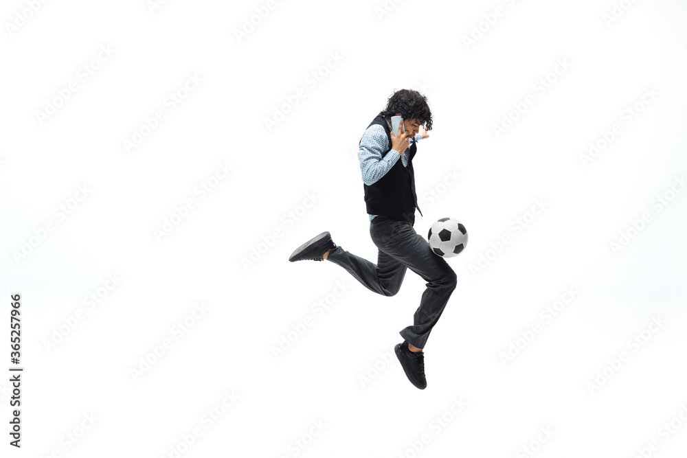 Man in office clothes playing football or soccer with ball on white background like professional player. Unusual look for businessman in jump kicking ball. Sport, healthy lifestyle, creativity.