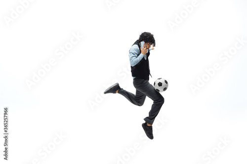 Man in office clothes playing football or soccer with ball on white background like professional player. Unusual look for businessman in jump kicking ball. Sport, healthy lifestyle, creativity. © master1305