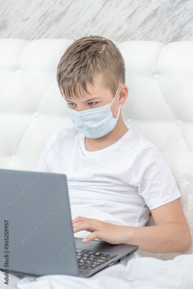 Sick boy wearing medical mask is engaged in distance learning with a laptop. Quarantine and coronavirus epidemic concept Sick boy wearing medical mask is engaged in distance learning with a laptop. Quarantine and coronavirus epidemic concept