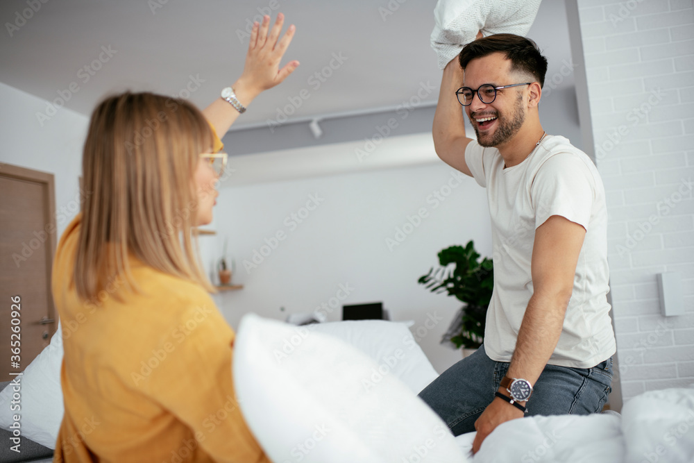 Obraz premium Young couple fighting pillows on the bed. Happy couple having fun at home. 