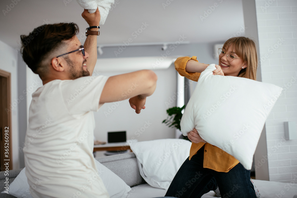 Fototapeta premium Young couple fighting pillows on the bed. Happy couple having fun at home. 