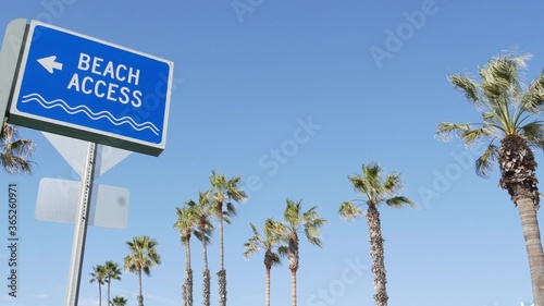 Beach sign and palms in sunny California, USA. Palm trees and seaside signpost. Oceanside pacific tourist resort aesthetic. Symbol of travel holidays and summertime vacations. Beachfront promenade