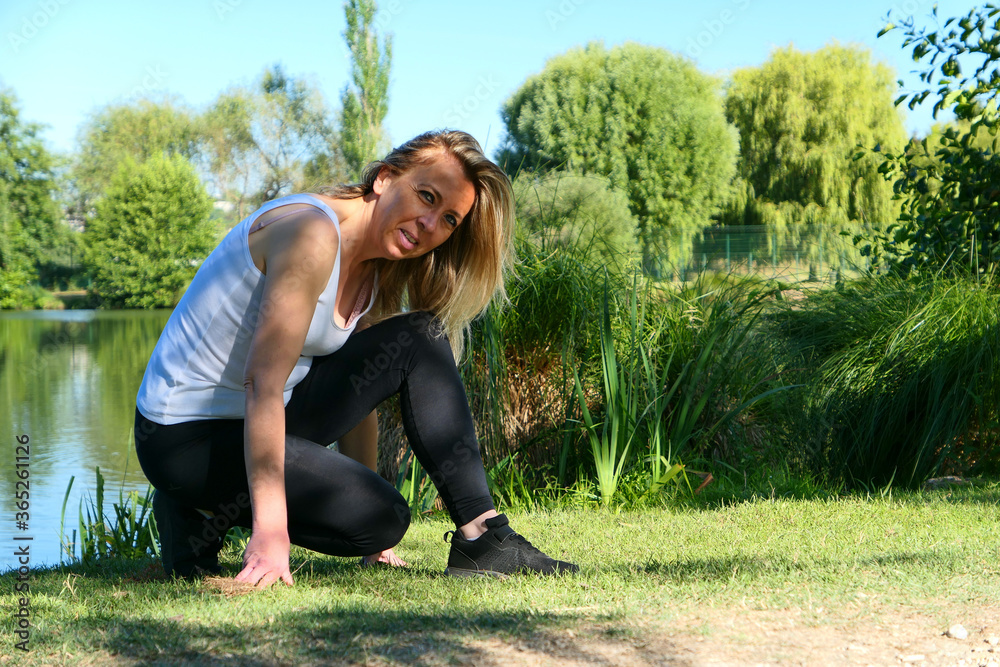 Smiling woman with long hair in fitness gear reattaching her sports shoe to the water's edge in nature on a summer day. Deliberately blurred background. Smiling woman with long hair in fitness gear reattaching her sports shoe to the water's edge in nature on a summer day. Deliberately blurred background.
