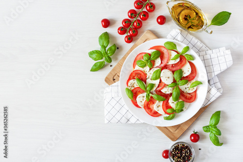 Caprese salad with mozzarela, tomatoes, fresh olive oil and basil on white background top view.