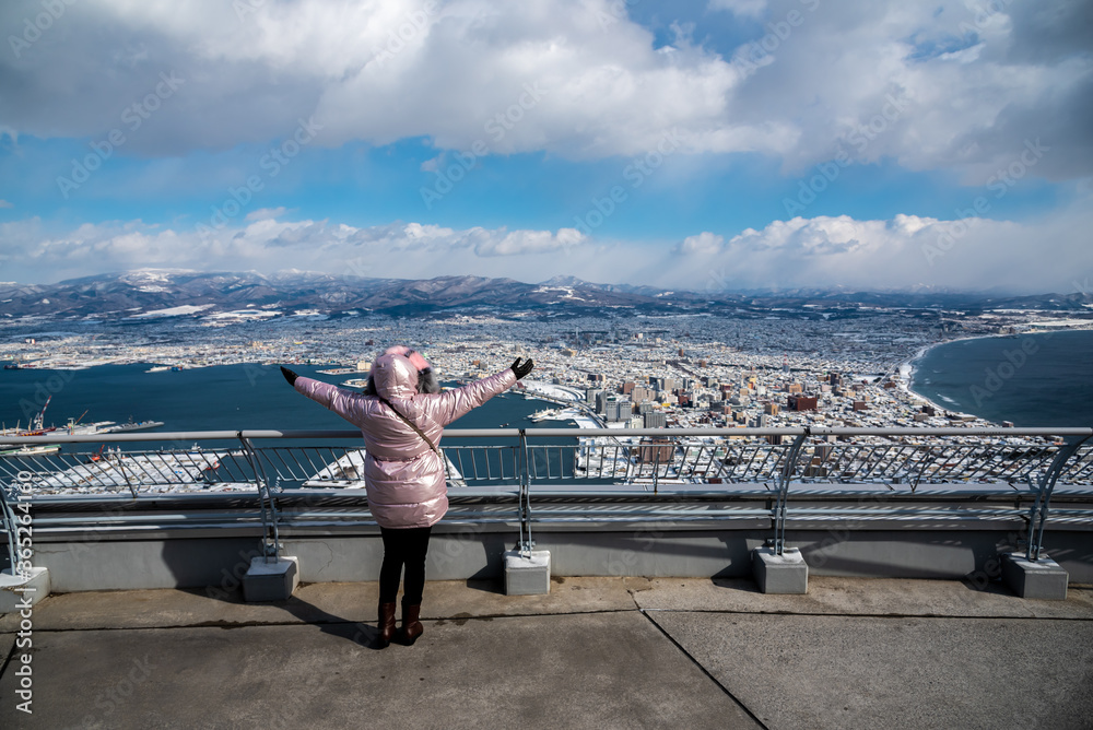 Traveler woman raised arms on the top of building to admire a beautiful city of Hakodate from height view in Japan.