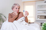 Sickness, coronavirus problem concept. Senior woman being sick having flu lying on sofa looking at temperature on thermometer. COVID19 pandemic
