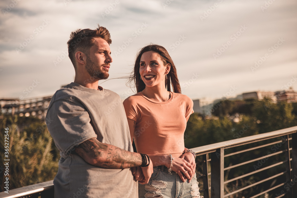 Young engaged couple posing serious and amused along the railing of an urban environment Young engaged couple posing serious and amused along the railing of an urban environment