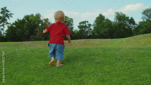 Toddler running on green grass. Blonde child playing in summer park