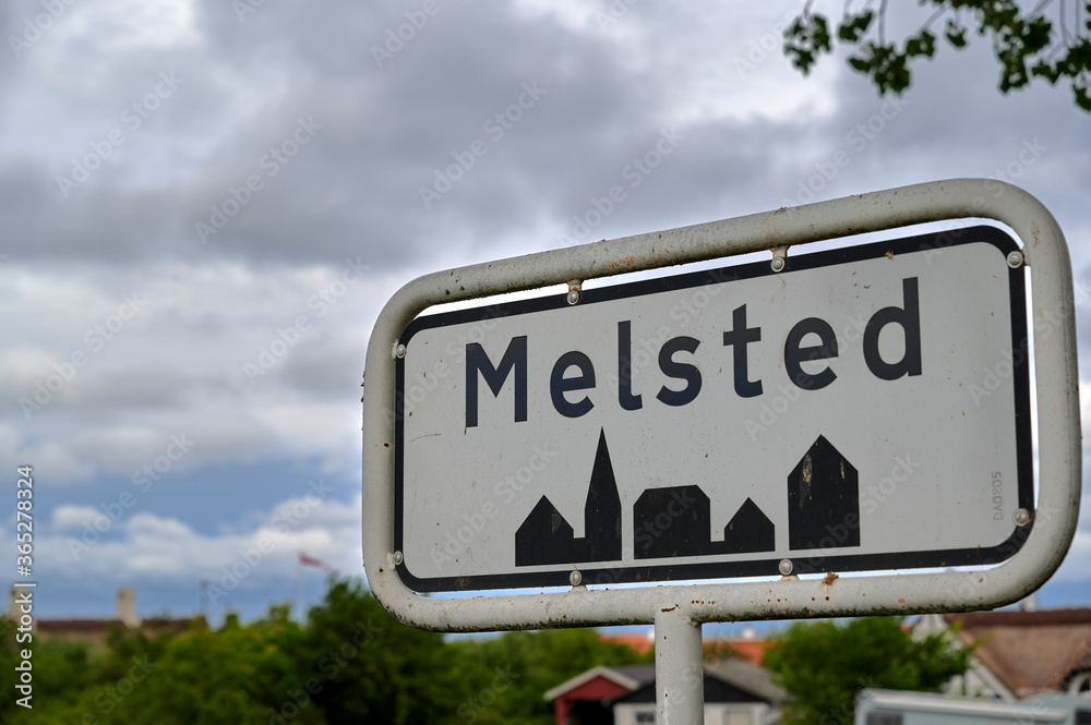 Ortsschild des Orts Melsted auf der dänischen Insel Bornholm vor einem bewölkten Himmel.