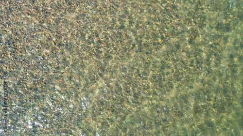 View of multicolored pebble of sea beach under clear water. Pattern of sea stone texture under water. Sea bottom with pebbles through clear water. Natural background.