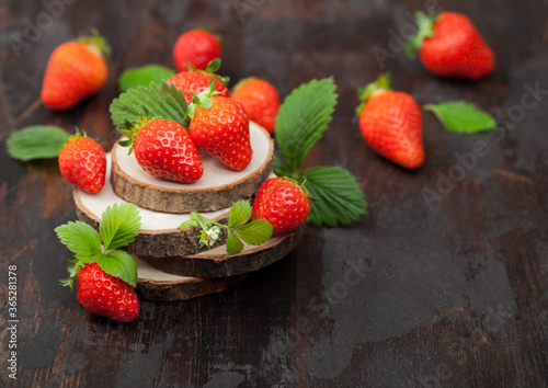 Organic fresh raw strawberries with leaf on timber round boards on dark background.