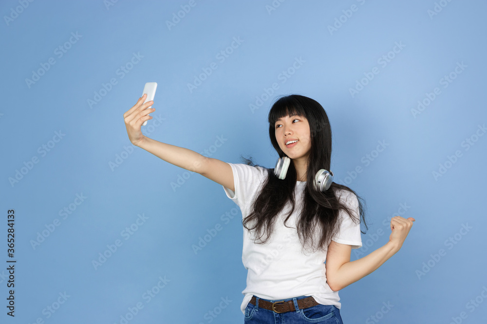 Taking selfie, vlog. Portrait of young asian woman isolated on blue studio background. Beautiful cute girl in casual. Human emotions, facial expression, sales, ad, online shopping concept. Taking selfie, vlog. Portrait of young asian woman isolated on blue studio background. Beautiful cute girl in casual. Human emotions, facial expression, sales, ad, online shopping concept.
