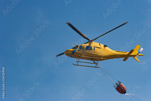 A fire helicopter carries water to put out a fire that has been caused by the heat of the summer.