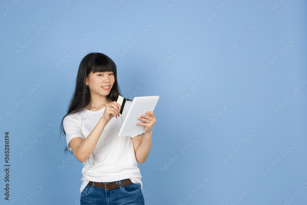 Showing tablet and card, purchase. Portrait of young asian woman isolated on blue studio background. Beautiful cute girl in casual. Human emotions, facial expression, sales, ad, online shopping Showing tablet and card, purchase. Portrait of young asian woman isolated on blue studio background. Beautiful cute girl in casual. Human emotions, facial expression, sales, ad, online shopping