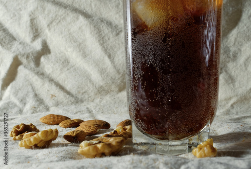 A glass of coke with ice and walnuts on a white tablecloth, taken with a hard light.