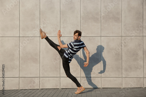 Jumping young buinessman in front of city building wall, on the run in jump high. Hurrying up, moving to daily routine inspired and sportive. Young ballet dancer in casual clothes and sunshine.