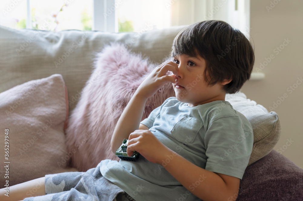 Kid lying on sofa scratching his nose while watching TV, Child feeling itchy on his nose from fluffy cushion, Young boy relaxing at home on his own in weekend. Positive children concept Kid lying on sofa scratching his nose while watching TV, Child feeling itchy on his nose from fluffy cushion, Young boy relaxing at home on his own in weekend. Positive children concept