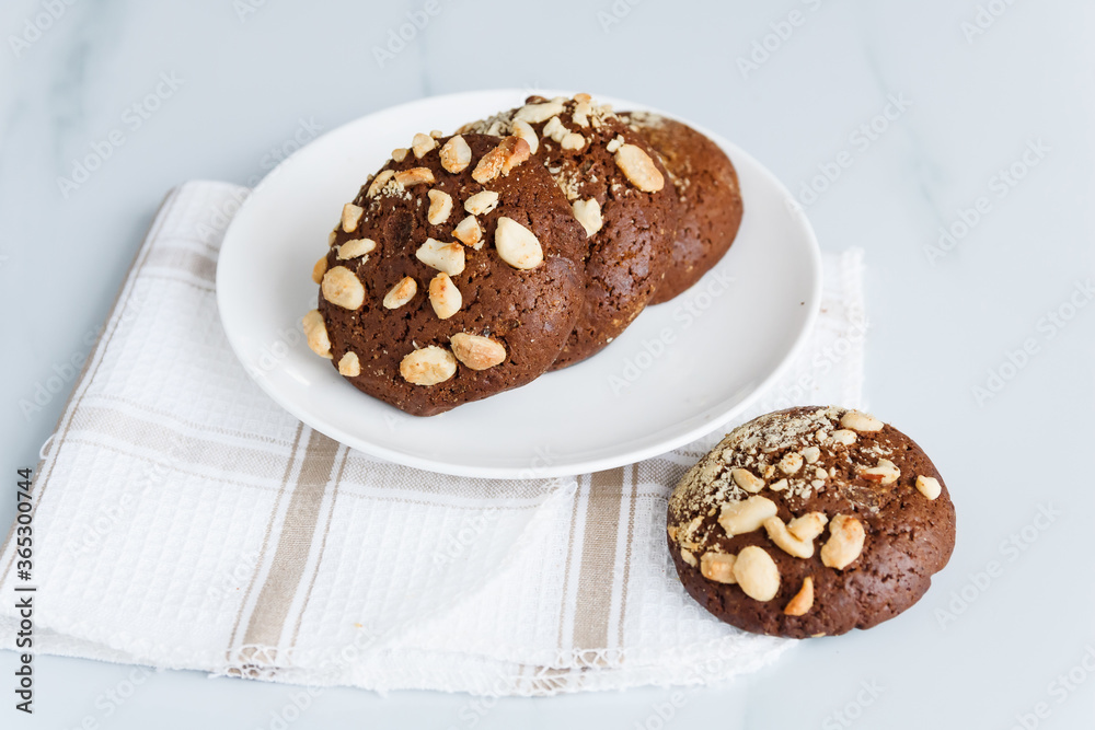 chocolate chip cookies with nuts and peanuts in a white tea plate on a table with a tea napkin chocolate chip cookies with nuts and peanuts in a white tea plate on a table with a tea napkin