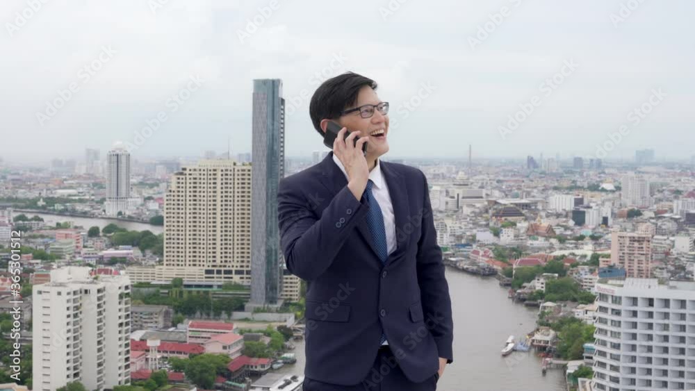 Happy young Asian businessman office worker using mobile phone discussion with colleague teamwork for success project. Successful business man entrepreneur working with wireless technology in the city Happy young Asian businessman office worker using mobile phone discussion with colleague teamwork for success project. Successful business man entrepreneur working with wireless technology in the city