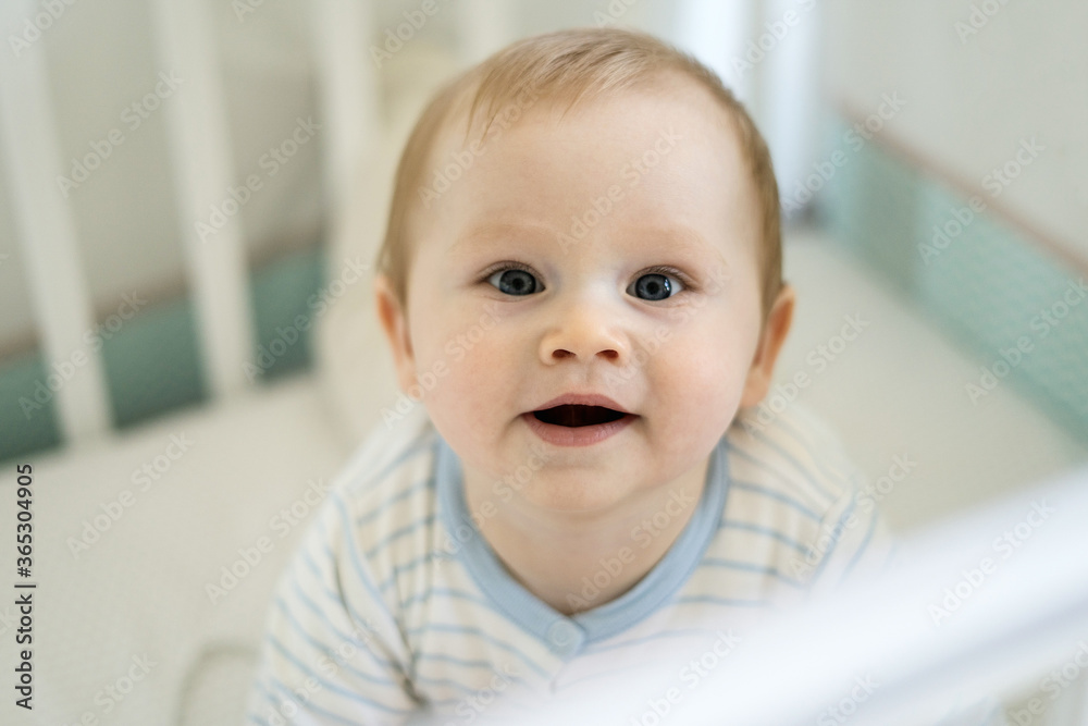 A six months old baby is smiling in the crib