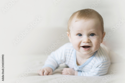 Cute six month old baby lying on his stomach on a bed on a beige background. Soft focus, copy space.