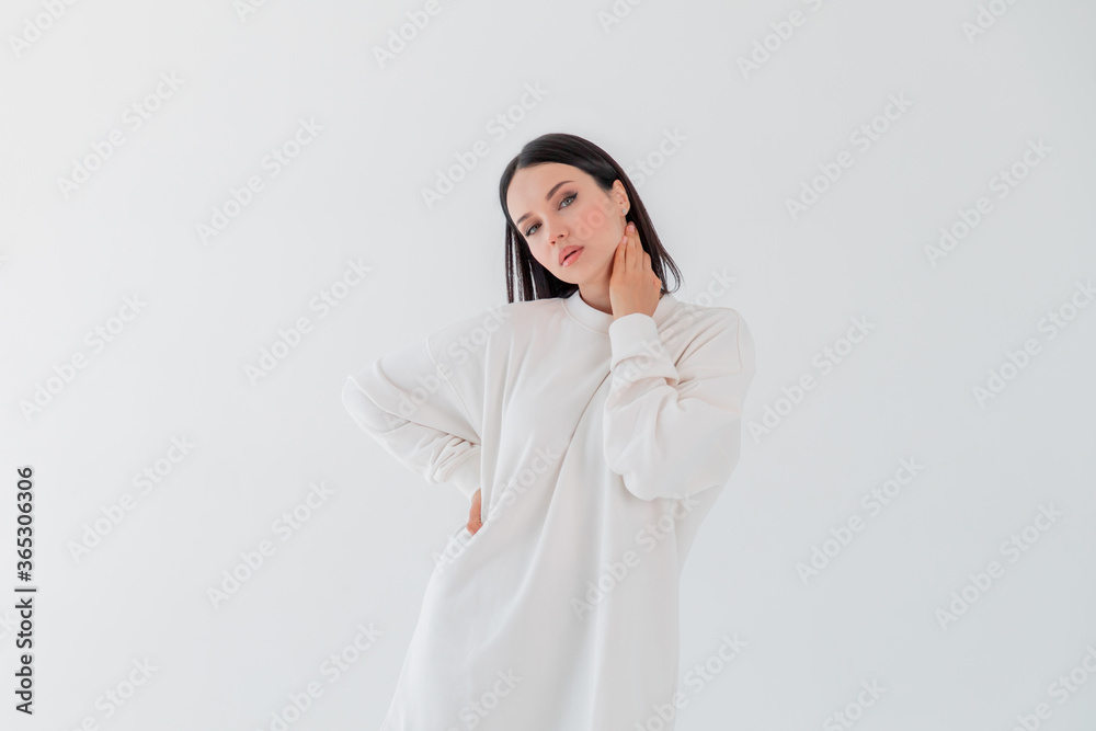 Hipster young girl over wall. Beautiful adult girl model in white sweater hoody isolated over gray white background Hipster young girl over wall. Beautiful adult girl model in white sweater hoody isolated over gray white background