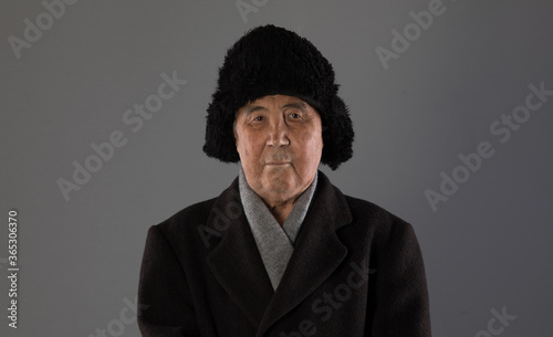 portrait of an old man in winter clothes on a gray background