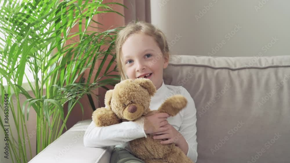 Girl sits on a sofa with her favorite toy in her hands and waves her hello foot. Girl sits on a sofa with her favorite toy in her hands and waves her hello foot.