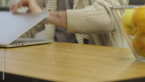 A man sitting at a table opens up his laptop and starts typing. Low shot showing only his hands and arms.