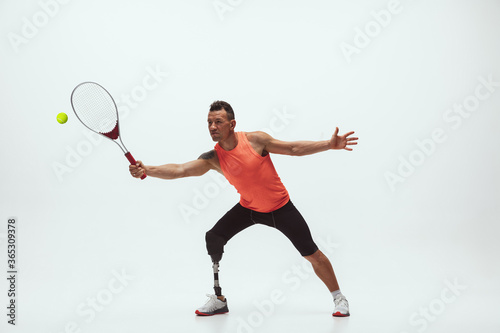 Athlete with disabilities or amputee isolated on white studio background. Professional male tennis player with leg prosthesis training in studio. Disabled sport and healthy lifestyle concept.