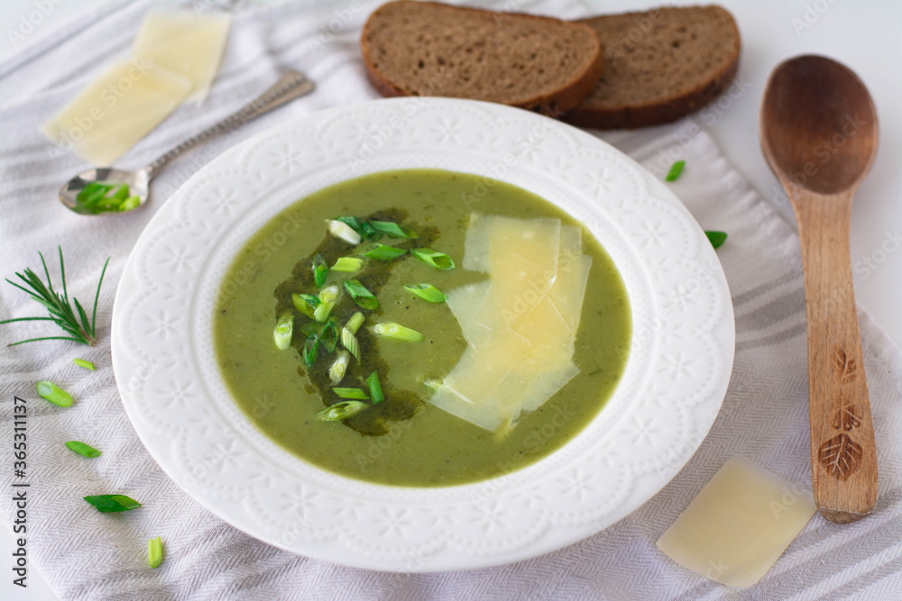 Soup of leeks, scallions green spring onions and potatoes garnished with pesto, scallions and shaved parmesan. In the background is black rye bread, wooden spoon and shaved parmesan Soup of leeks, scallions green spring onions and potatoes garnished with pesto, scallions and shaved parmesan. In the background is black rye bread, wooden spoon and shaved parmesan