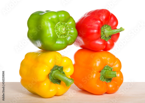 Close up of bell peppers on a light wood table side by side and stacked. Green, yellow, orange and red.