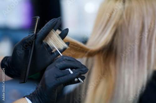 A hairdresser in rubber gloves holds a pair of scissors and a comb. Woman getting a new haircut.