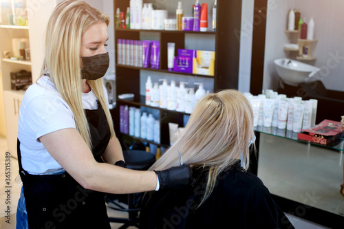 Hairdresser with security measures for Covid-19, a woman in a medical mask, social distance, cutting hair with a medical mask and rubber gloves in a beauty salon.