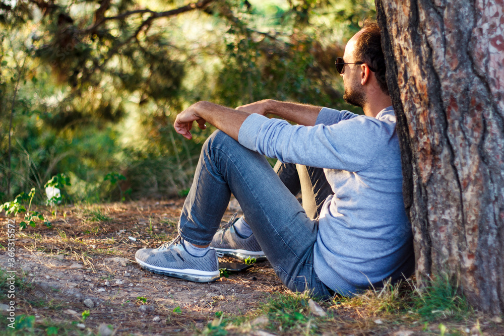 Single man sitting under a tree, watching his view, resting and enjoying the moment Single man sitting under a tree, watching his view, resting and enjoying the moment