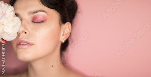  Girl with pink makeup with a peony in her hands on a pink background 