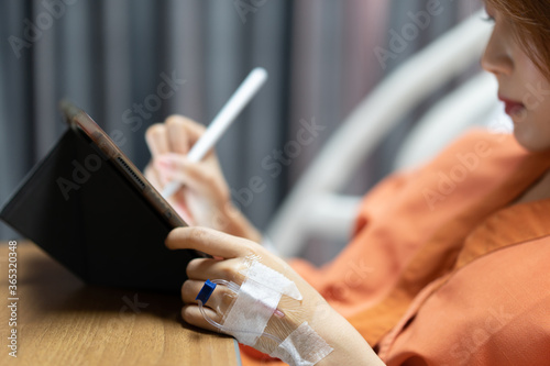 young asian girl is wearing an orange patient gown. lying in the hospital bed writing on tablet screen