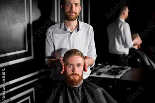 Master cuts hair and beard in the Barber shop. Hairdresser makes hairstyle using scissors and a metal comb. Not satisfied with the work of the client.