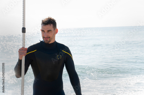 attractive and athlete  guy in wetsuit stretches on the beach before entering the sea with the surfboard