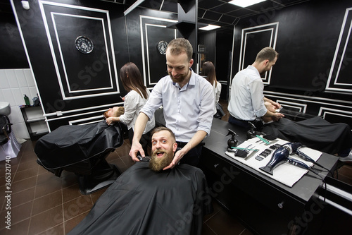 Master cuts hair and beard of men in the barbershop, hairdresser makes hairstyle for a young man